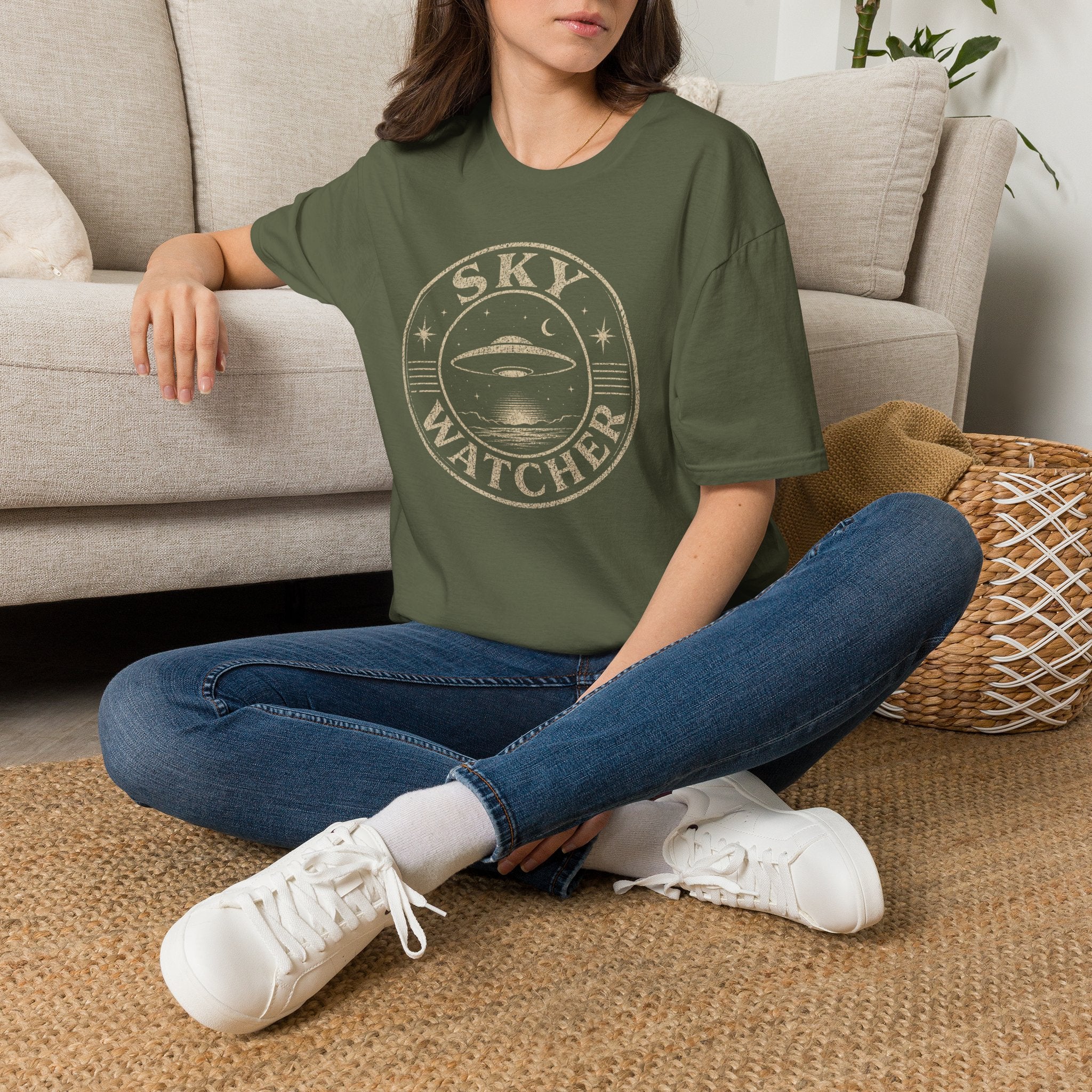 Person wearing green retro UFO t-shirt with a distressed circular badge showing a flying saucer over water at night with a crescent moon and the words SKY WATCHER in pale lettering