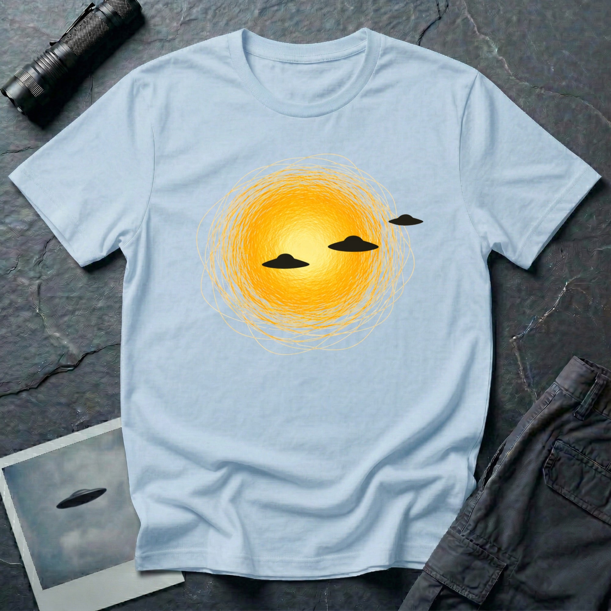 Solar Fly-by artistic UFO t-shirt — three black flying saucers passing across a glowing sun on light blue unisex cotton tee