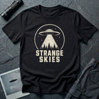 Black retro UFO t-shirt with a flying saucer and tractor beam over a conifer forest inside a distressed circle with the words STRANGE SKIES in white