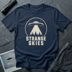 Navy blue retro UFO t-shirt with a flying saucer and tractor beam over a conifer forest inside a distressed circle with the words STRANGE SKIES in white