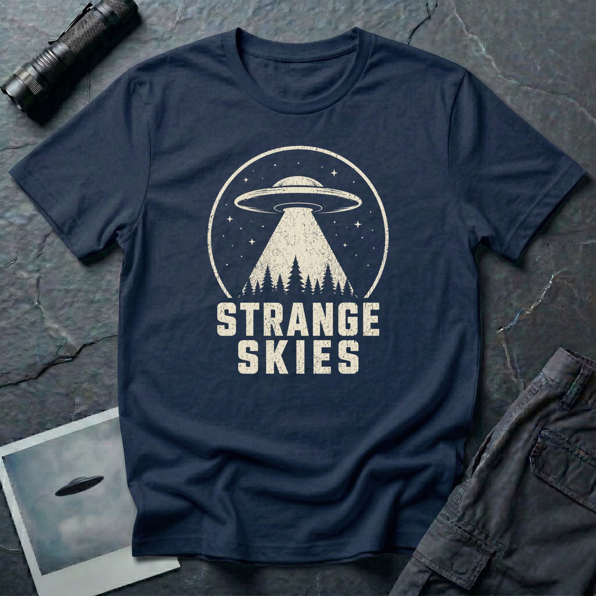 Navy blue retro UFO t-shirt with a flying saucer and tractor beam over a conifer forest inside a distressed circle with the words STRANGE SKIES in white