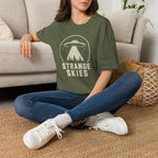 Person wearing retro UFO t-shirt with a flying saucer and tractor beam over a conifer forest inside a distressed circle with the words STRANGE SKIES in white