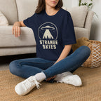 Person wearing navy blue retro UFO t-shirt with a flying saucer and tractor beam over a conifer forest inside a distressed circle with the words STRANGE SKIES in white