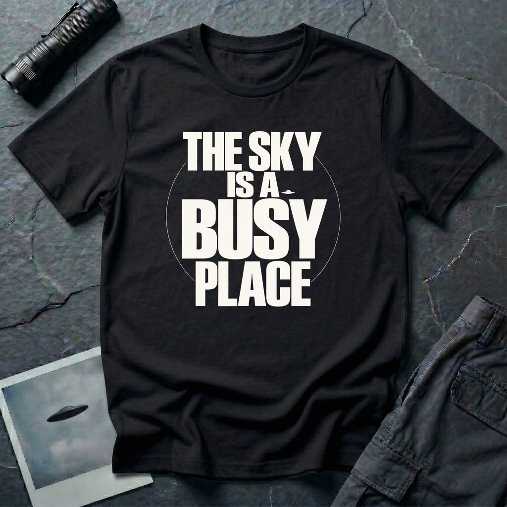 Black t-shirt with bold white text reading The Sky Is A Busy Place and small UFO silhouette