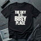 Black t-shirt with bold white text reading The Sky Is A Busy Place and small UFO silhouette
