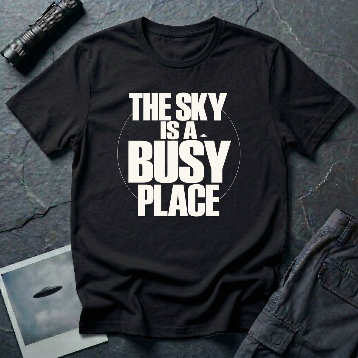 Black t-shirt with bold white text reading The Sky Is A Busy Place and small UFO silhouette