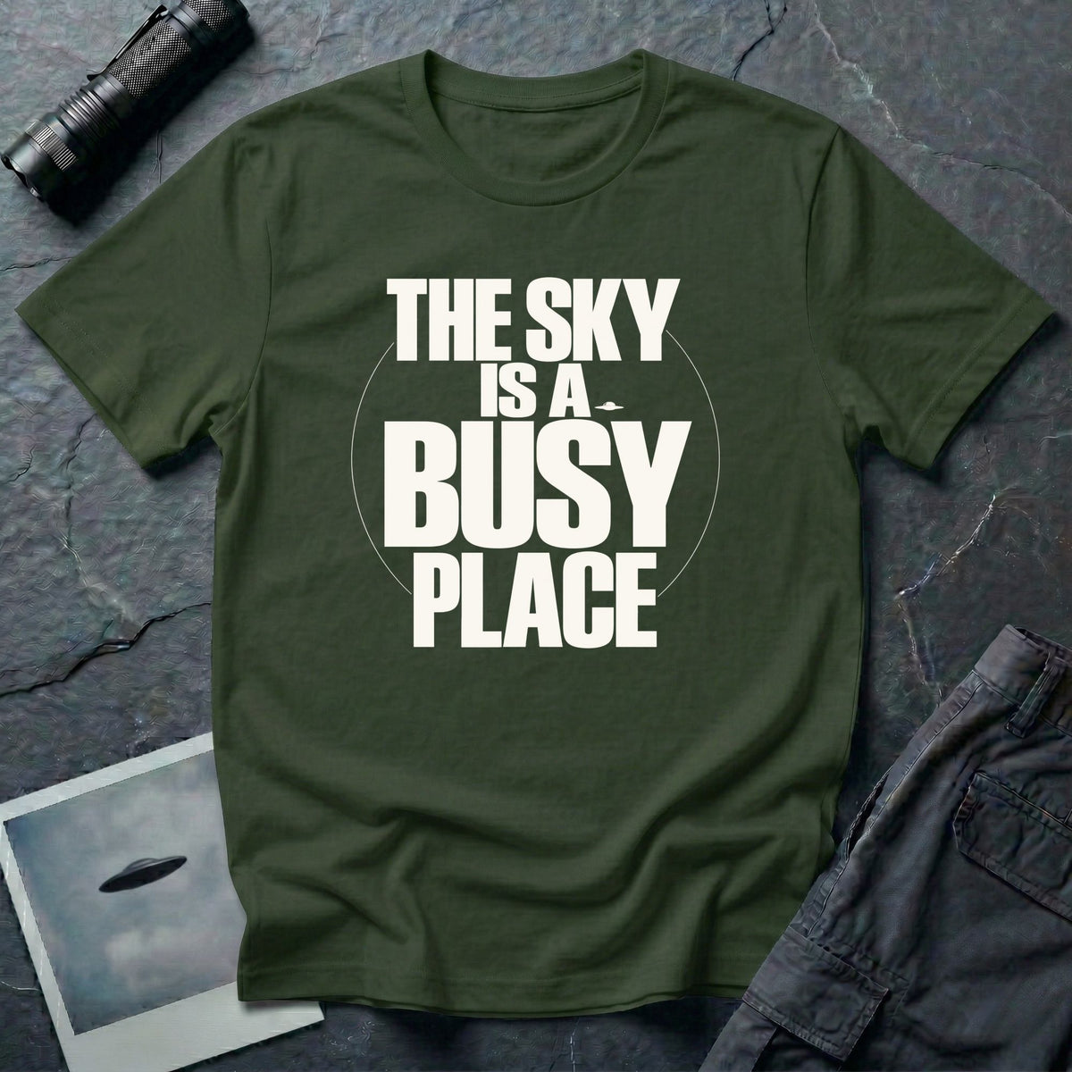 Military green t-shirt with bold white text reading The Sky Is A Busy Place and small UFO silhouette