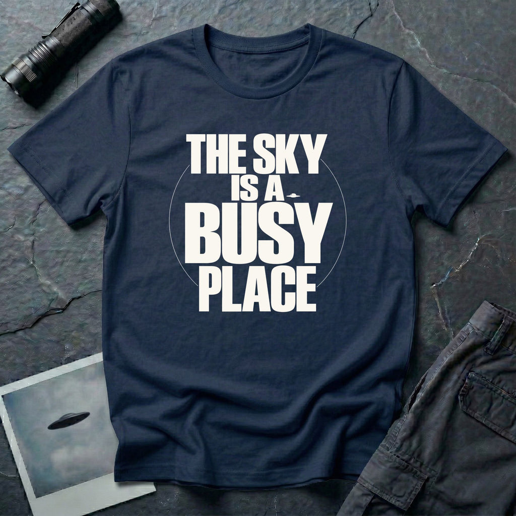 Navy blue t-shirt with bold white text reading The Sky Is A Busy Place and small UFO silhouette