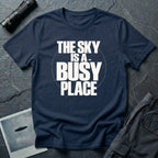 Navy blue t-shirt with bold white text reading The Sky Is A Busy Place and small UFO silhouette