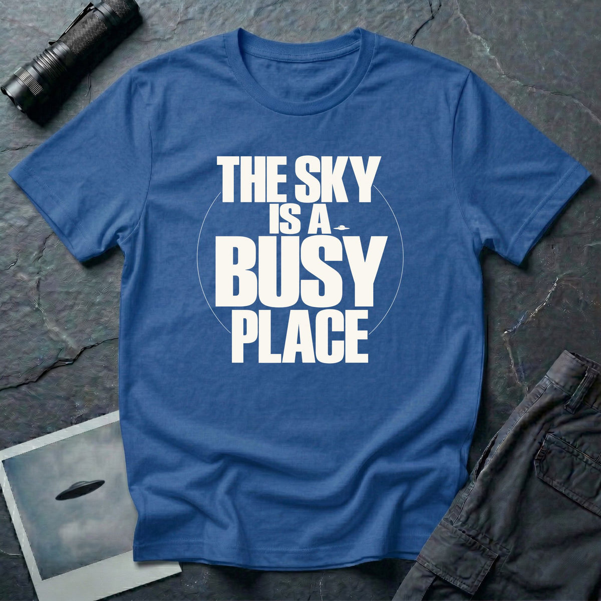 Royal blue t-shirt with bold white text reading The Sky Is A Busy Place and small UFO silhouette