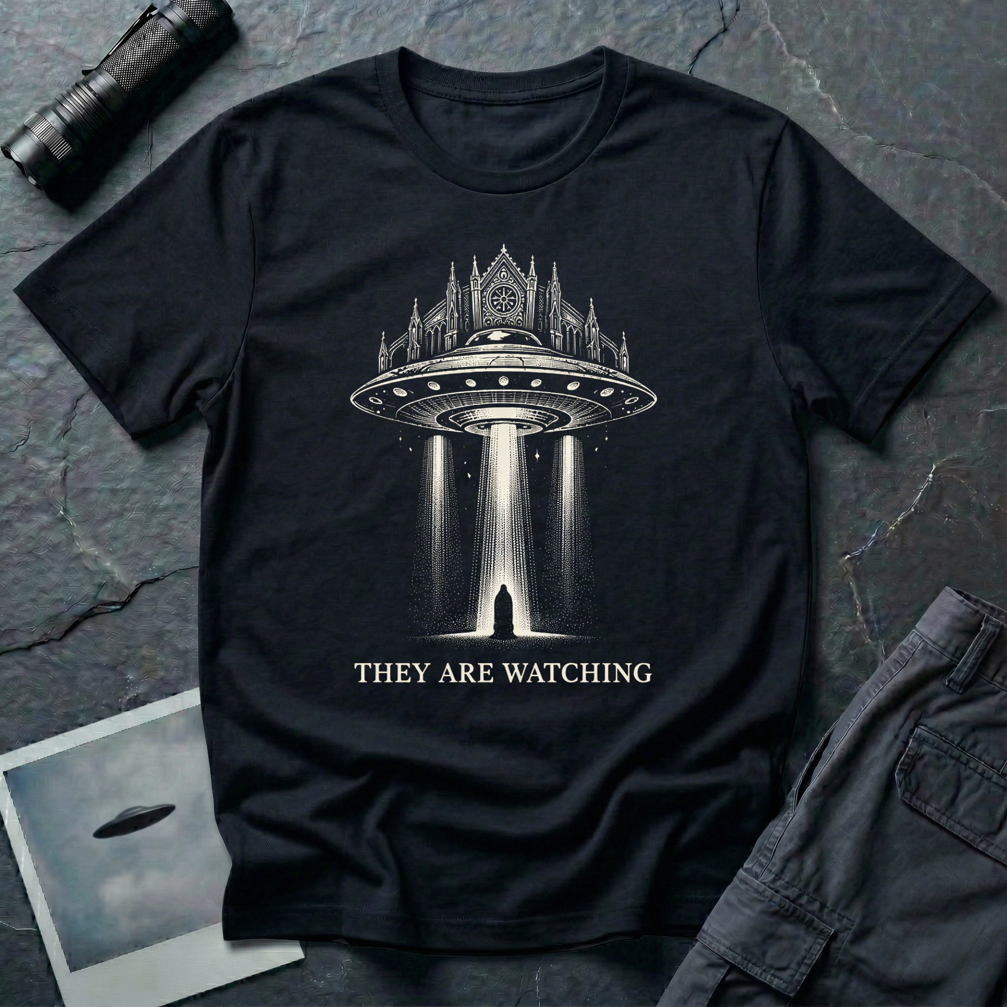 They Are Watching Gothic UFO t-shirt — medieval cathedral fused with flying saucer beaming down on hooded figure in cream line-work on black cotton tee