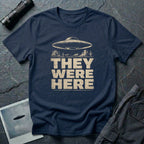 Navy blue retro UFO t-shirt with a flying saucer over a southwest desert landscape with mesa formations and cacti and the words THEY WERE HERE in distressed pale block letters