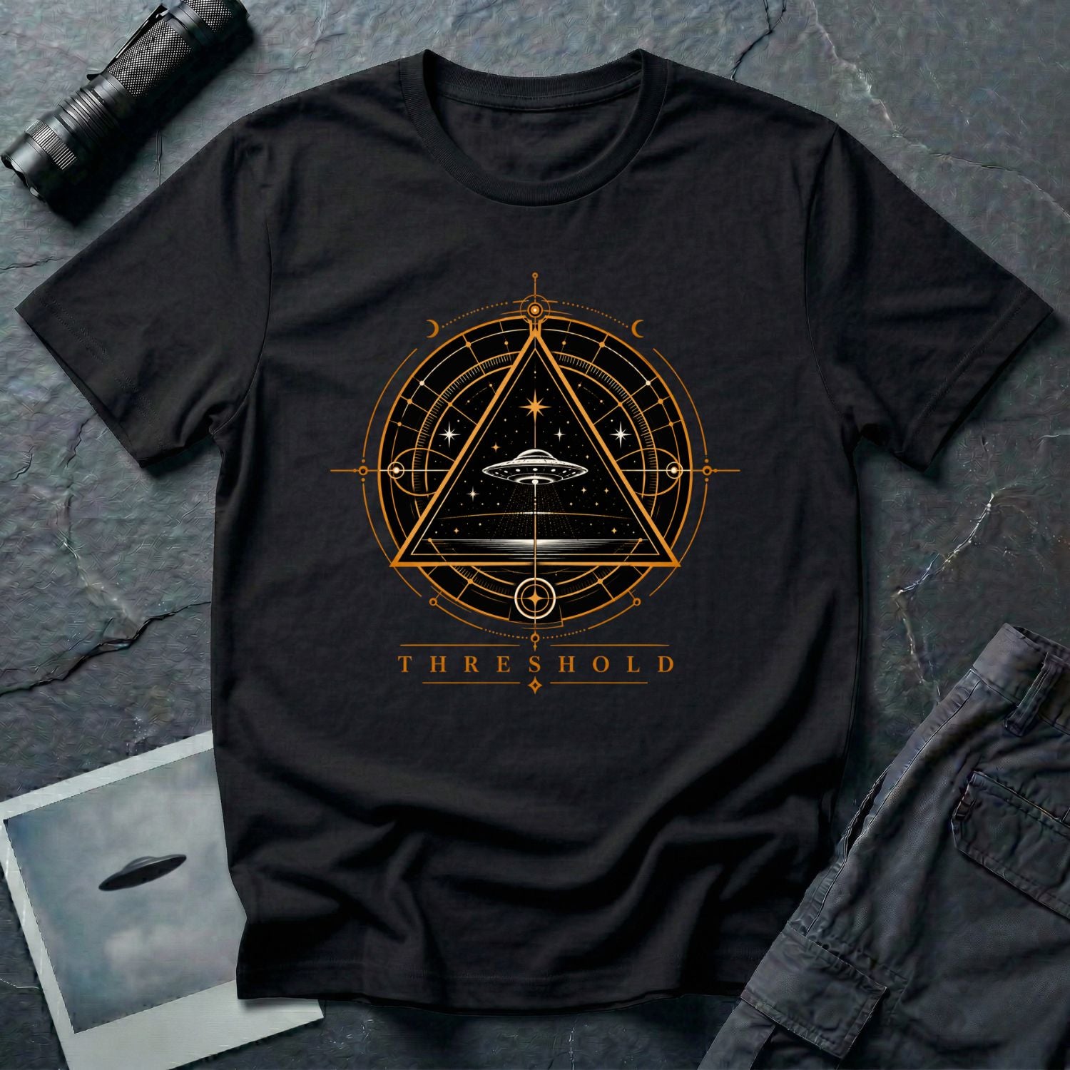 Black UFO t-shirt with a flying saucer inside an upward-pointing triangle portal with perspective grid, crescent moons, and compass frame in gold and black with the word THRESHOLD