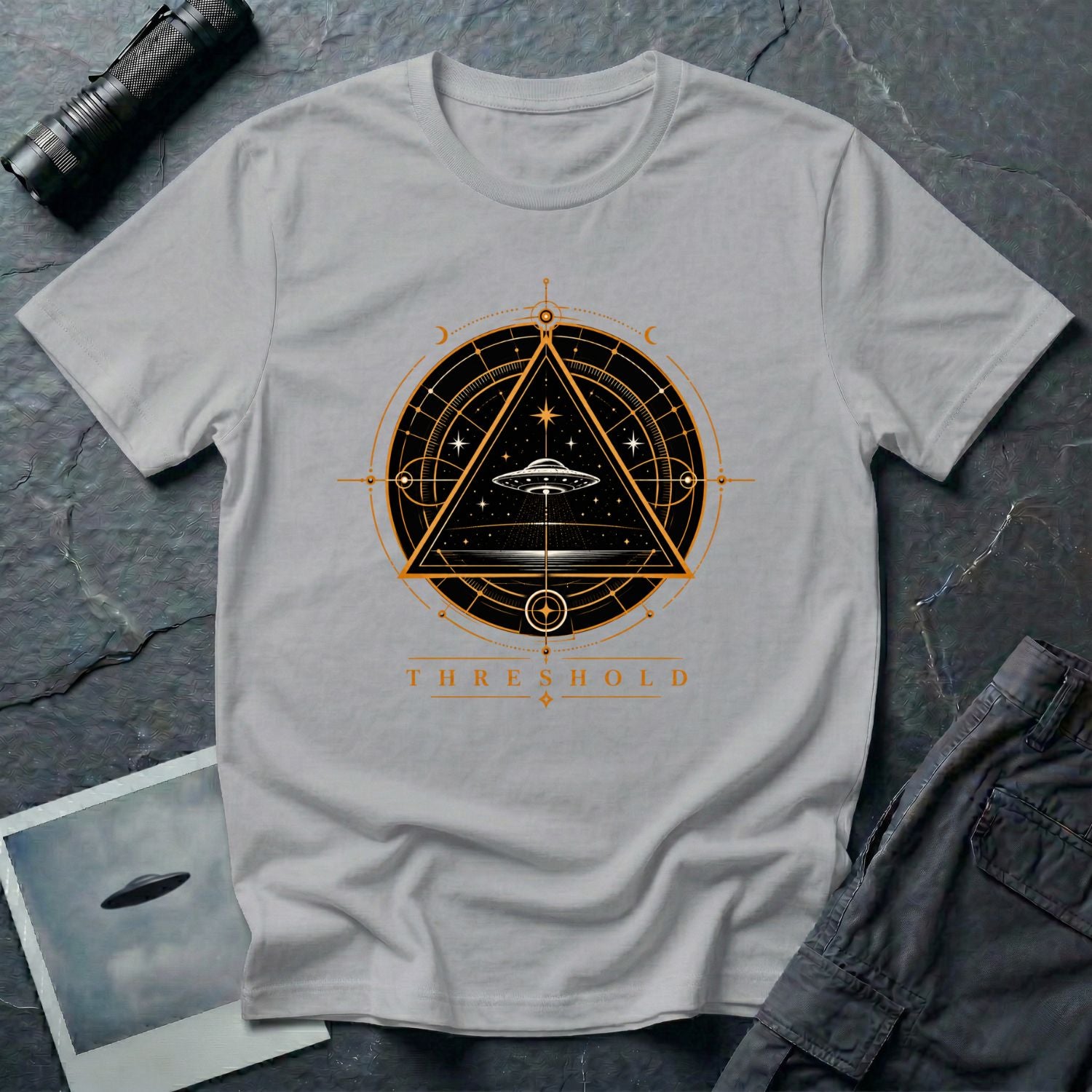 Grey UFO t-shirt with a flying saucer inside an upward-pointing triangle portal with perspective grid, crescent moons, and compass frame in gold and black with the word THRESHOLD