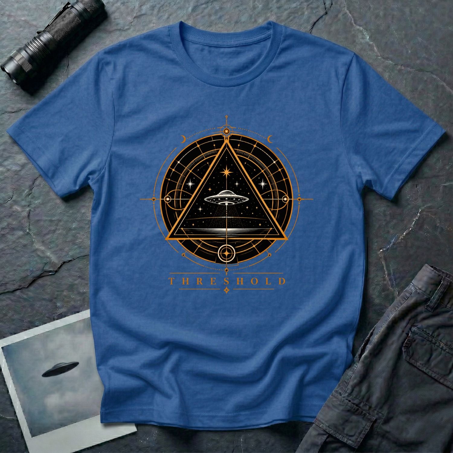 Royal blue UFO t-shirt with a flying saucer inside an upward-pointing triangle portal with perspective grid, crescent moons, and compass frame in gold and black with the word THRESHOLD
