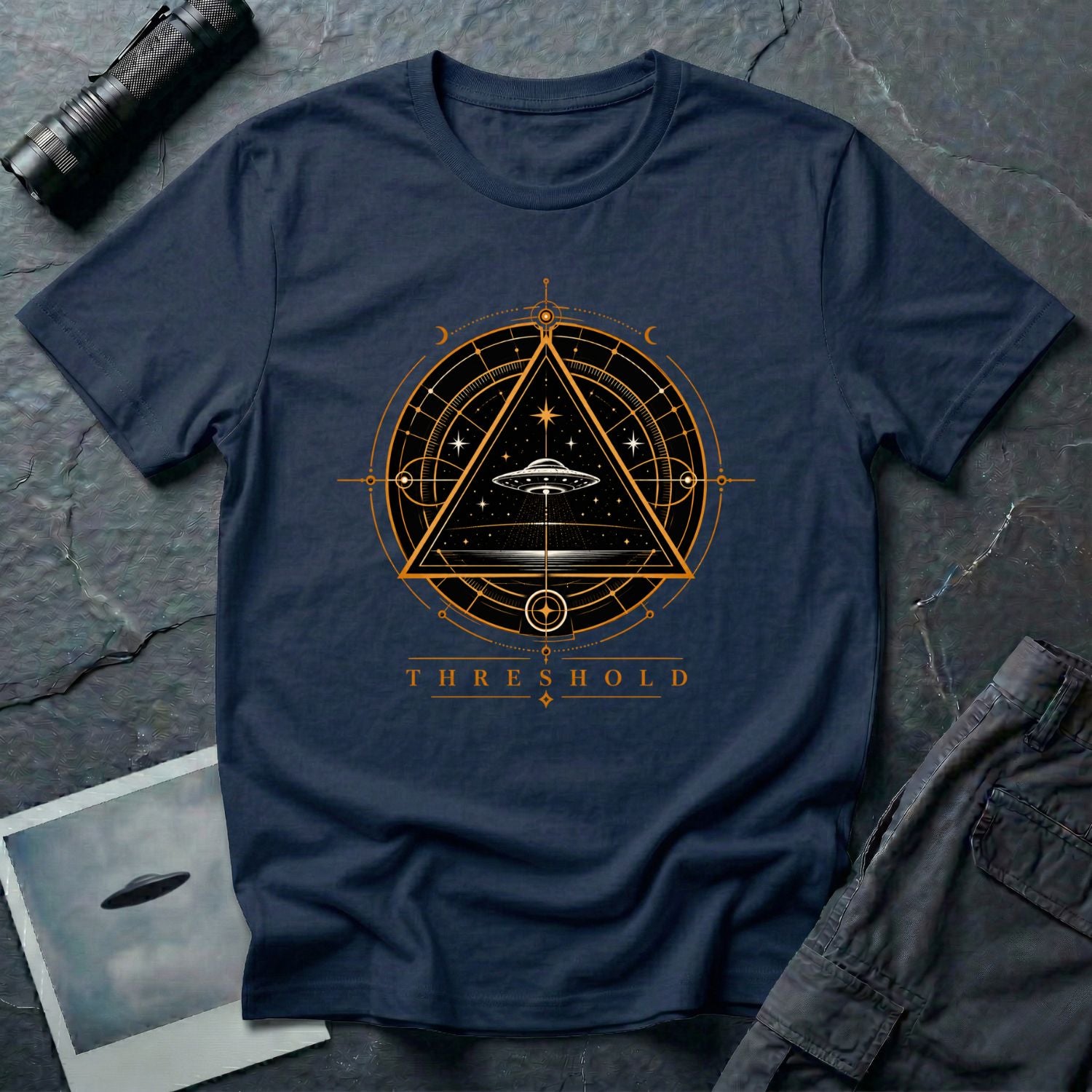 Navy blue UFO t-shirt with a flying saucer inside an upward-pointing triangle portal with perspective grid, crescent moons, and compass frame in gold and black with the word THRESHOLD
