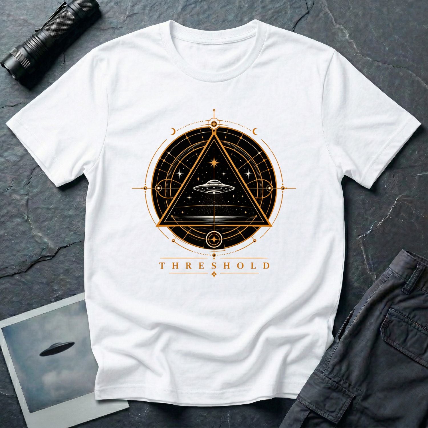 White UFO t-shirt with a flying saucer inside an upward-pointing triangle portal with perspective grid, crescent moons, and compass frame in gold and black with the word THRESHOLD