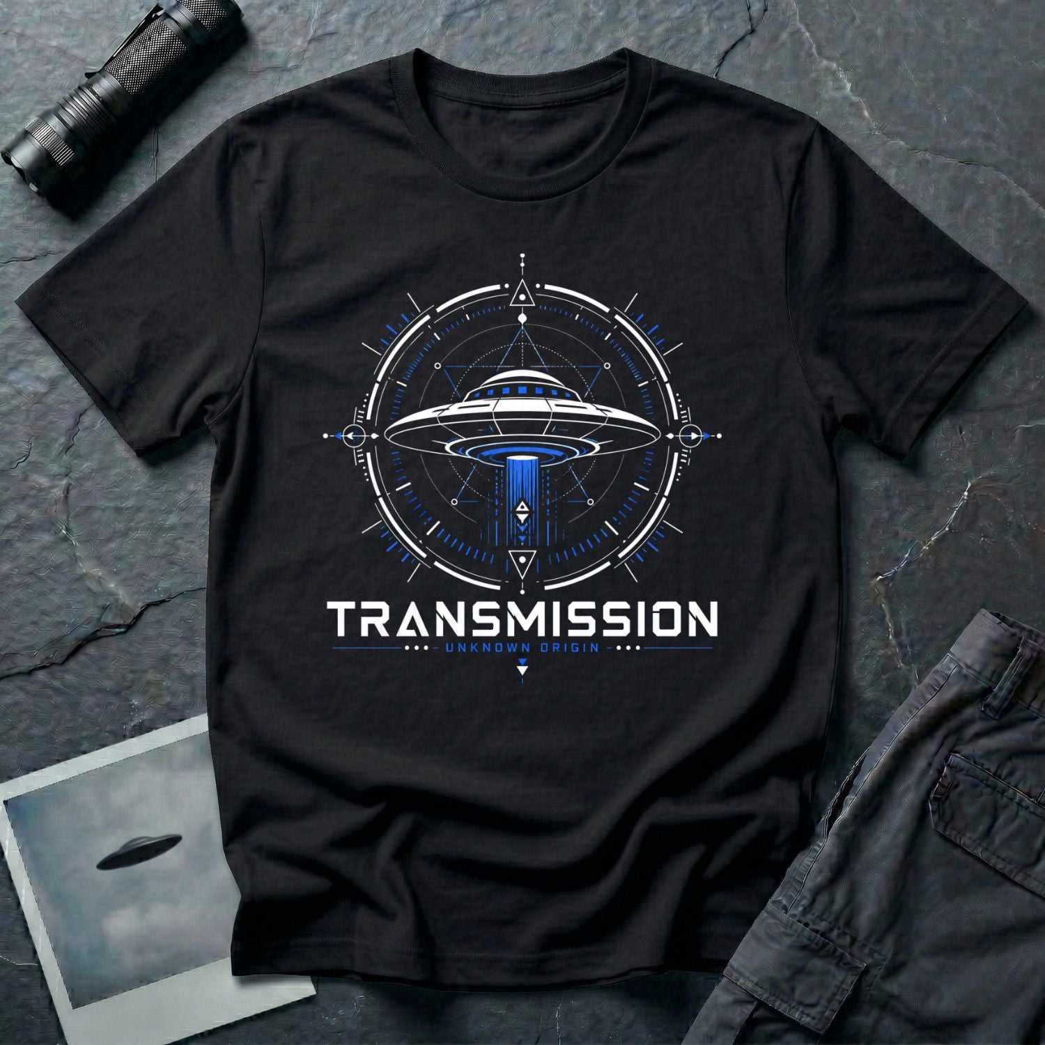 Black UFO t-shirt with a flying saucer inside a sacred geometry compass and the words "TRANSMISSION · UNKNOWN ORIGIN ·" in white and blue