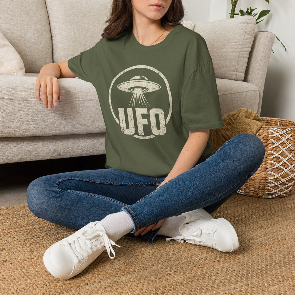 Person wearing green retro UFO t-shirt with a distressed circle containing a flying saucer with tractor beam and bold block letters spelling UFO in white