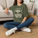 Person wearing green retro UFO t-shirt with a distressed circle containing a flying saucer with tractor beam and bold block letters spelling UFO in white