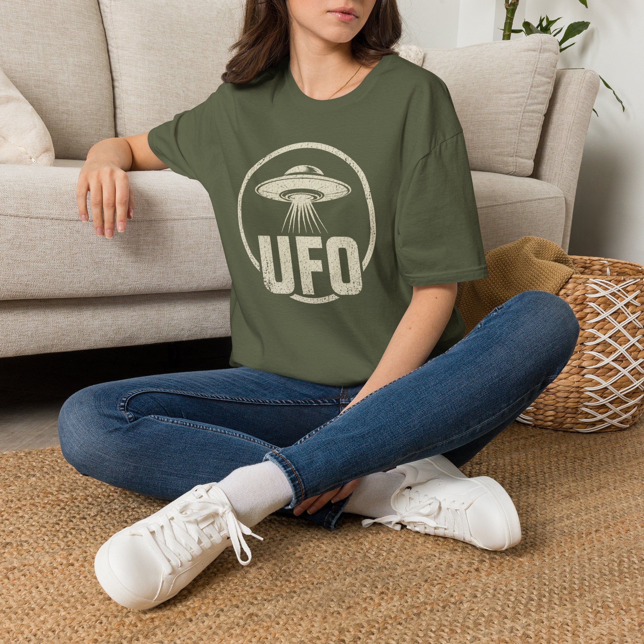 Person wearing green retro UFO t-shirt with a distressed circle containing a flying saucer with tractor beam and bold block letters spelling UFO in white