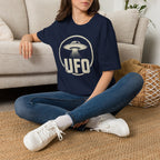 Person wearing blue retro UFO t-shirt with a distressed circle containing a flying saucer with tractor beam and bold block letters spelling UFO in white