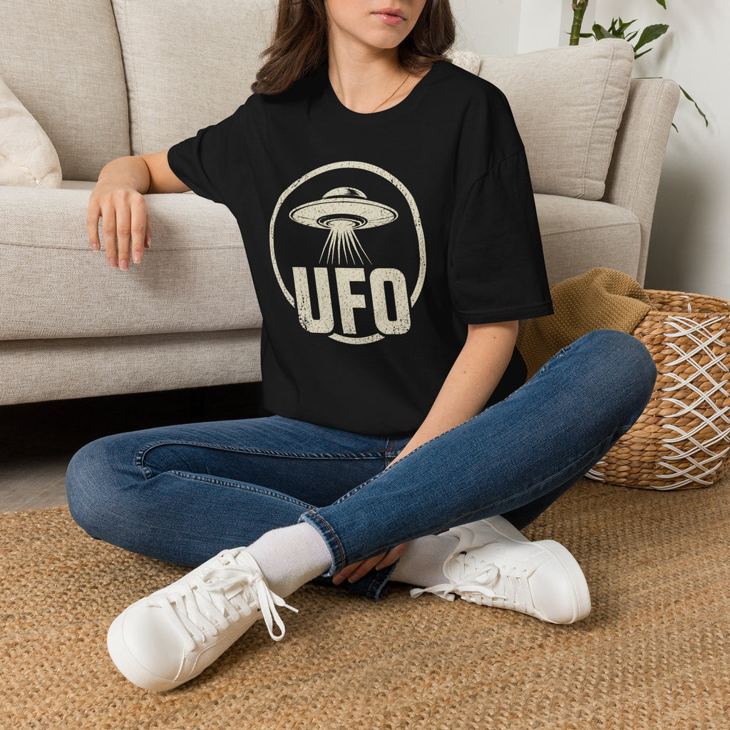 Person wearing black retro UFO t-shirt with a distressed circle containing a flying saucer with tractor beam and bold block letters spelling UFO in white