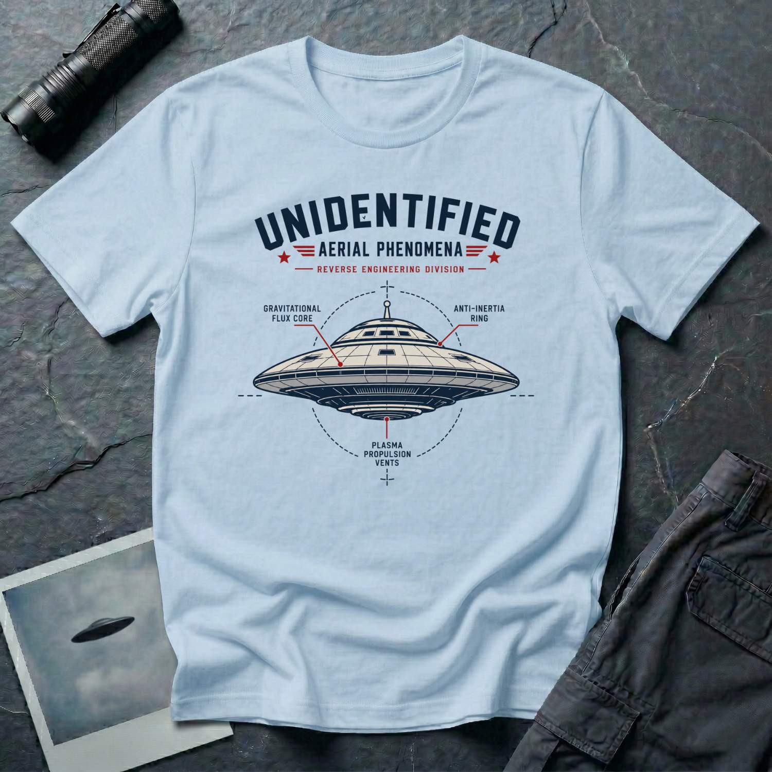 Pale blue t-shirt with military-style UAP Reverse Engineering Division patch featuring an annotated saucer diagram with gravitational flux core anti-inertia ring and plasma propulsion vents callouts