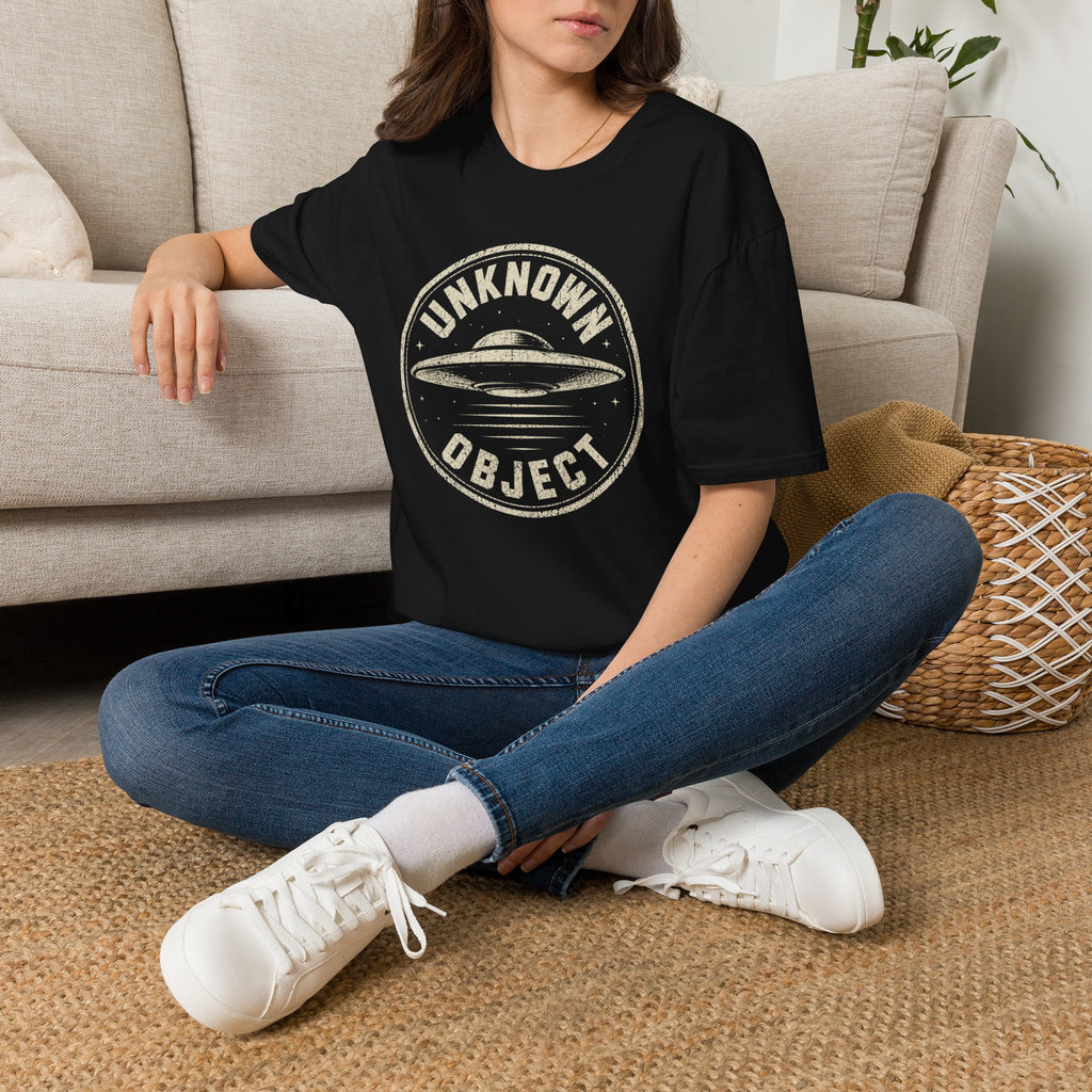 Person wearing black retro UFO t-shirt with a distressed circular badge showing a flying saucer with speed lines and the words UNKNOWN OBJECT in white