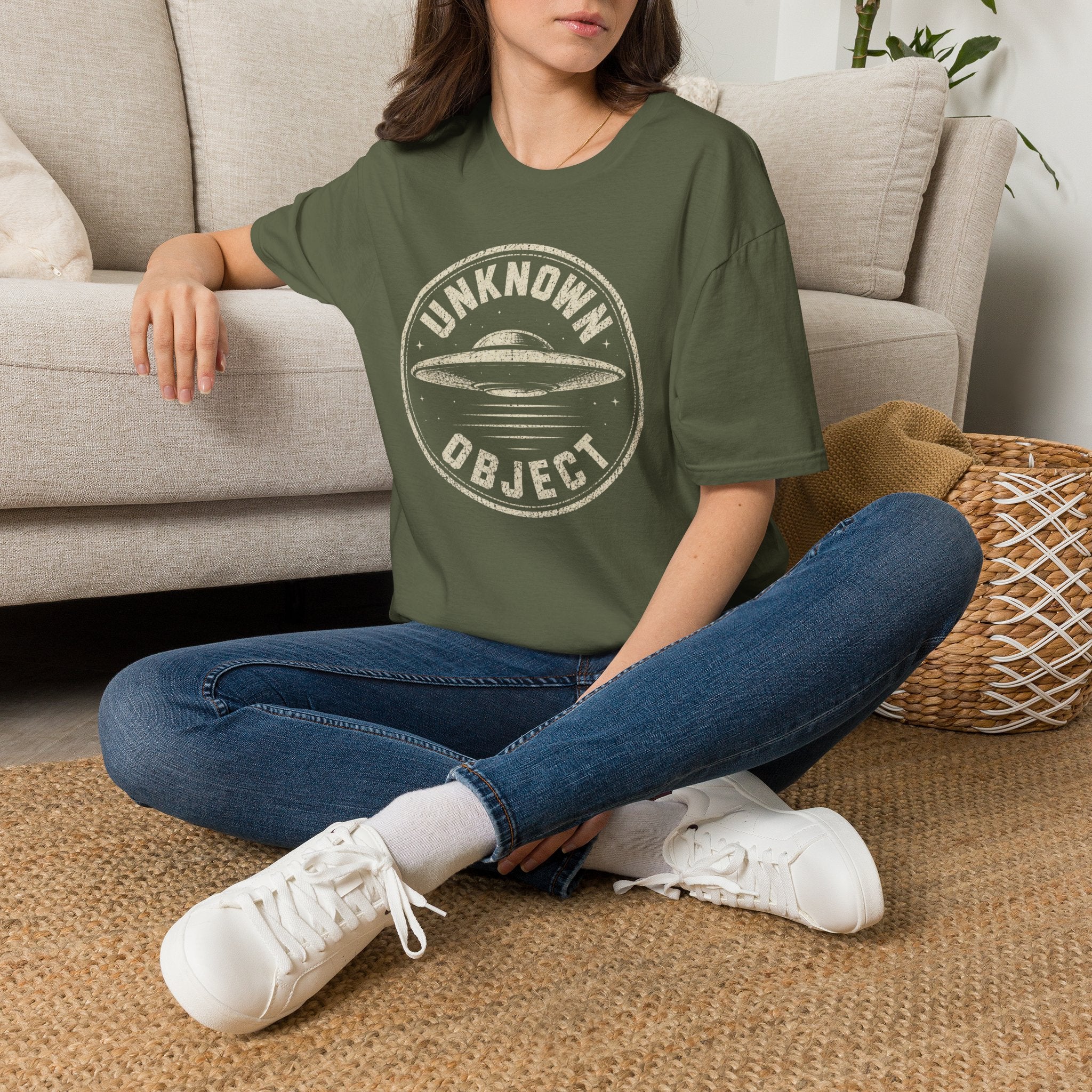 Person wearing green retro UFO t-shirt with a distressed circular badge showing a flying saucer with speed lines and the words UNKNOWN OBJECT in white