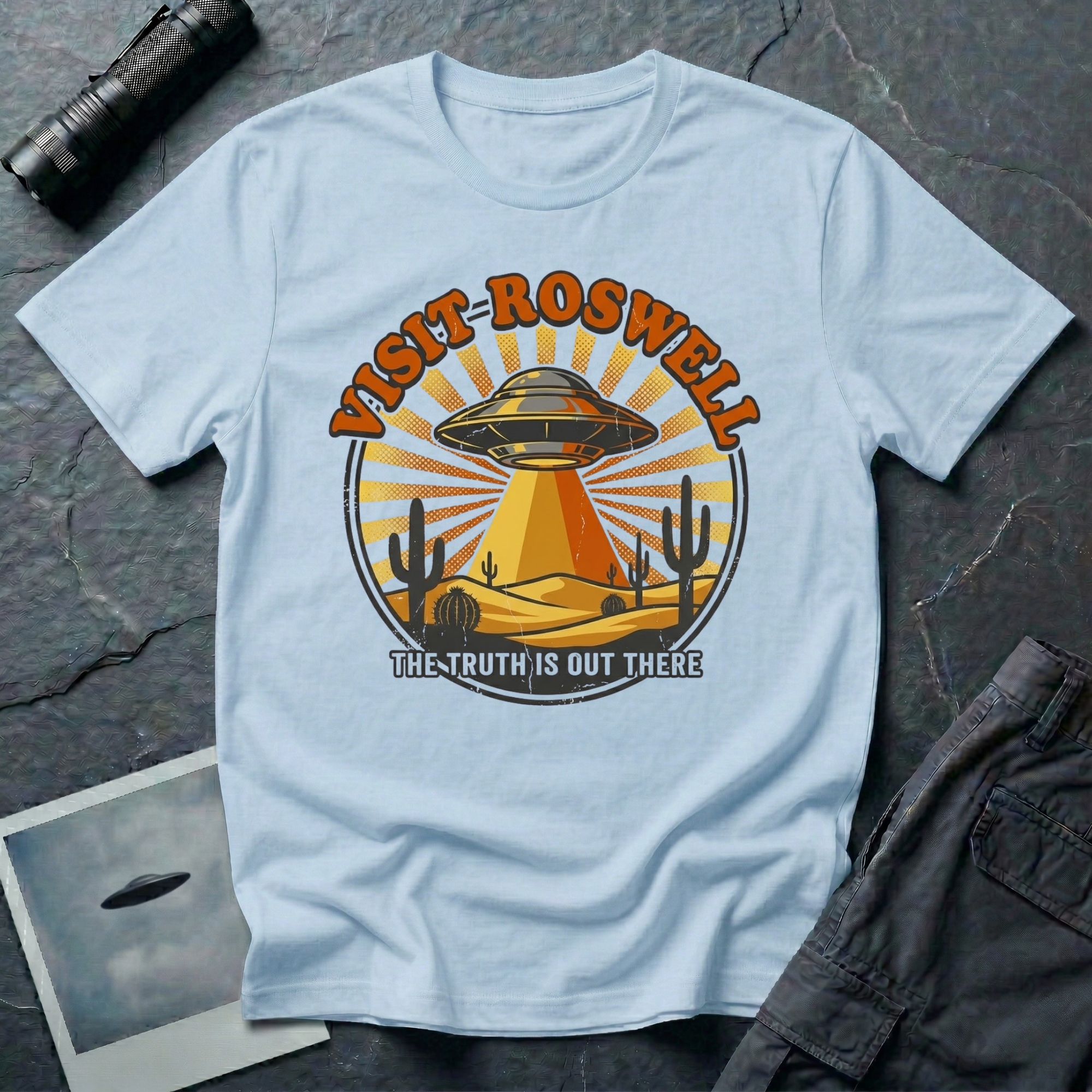 Visit Roswell UFO t-shirt — vintage circular tourism badge with flying saucer beaming over desert cacti in rust and mustard tones on light blue cotton tee